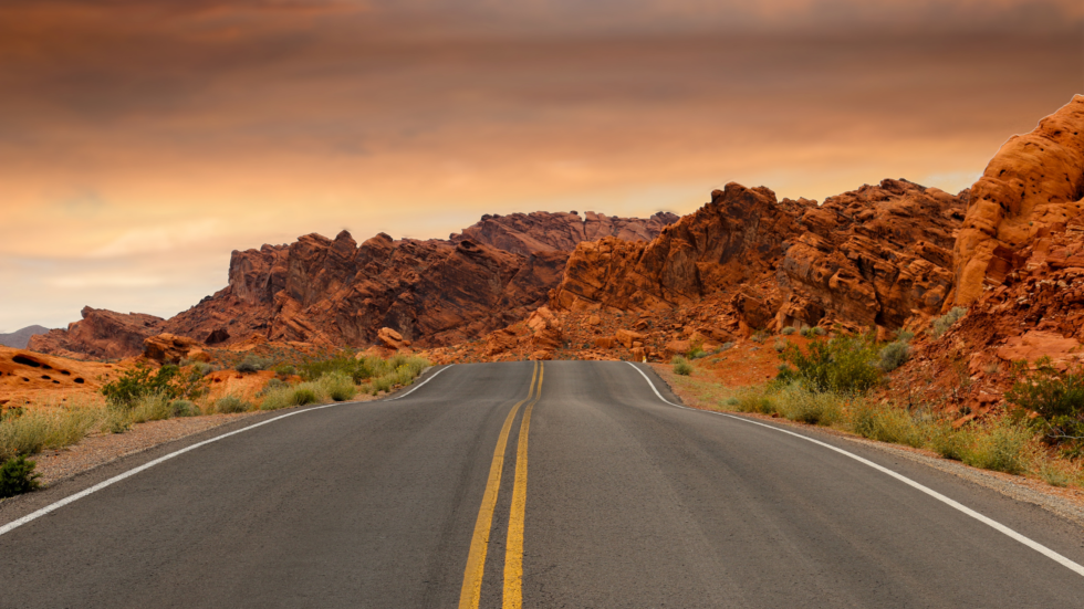 Desert road winding through rocky landscape at sunset.