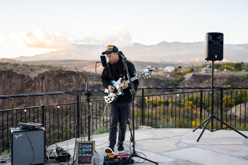 Musician playing guitar outdoors with mountain background.