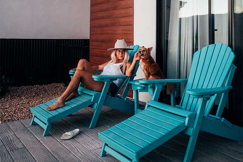 Woman relaxing with dog on blue Adirondack chairs.