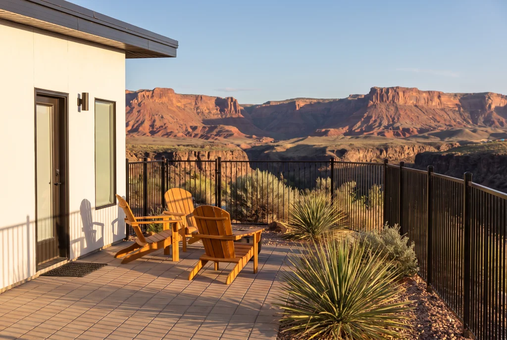 Two wooden chairs on a private patio at The Dwellings in La Verkin, with a black fence and red-rock canyon views.