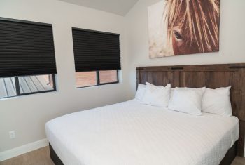 Modern bedroom with horse artwork and black blinds.