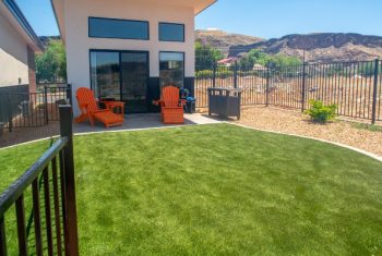 Backyard with artificial grass and orange Adirondack chairs.