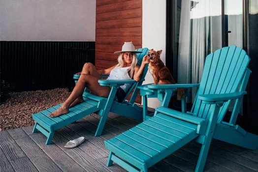 Woman relaxing with dog on blue Adirondack chairs.