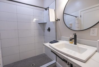 Modern white tiled bathroom with round mirror.